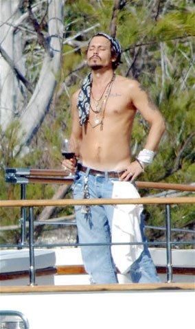 Johnny Depp shirtless on a boat facing up with a glass of red wine in his hand