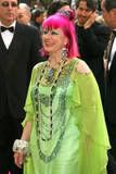 Woman with bright red hair, overdone clownish makeup, a bright green dress and multiple necklaces