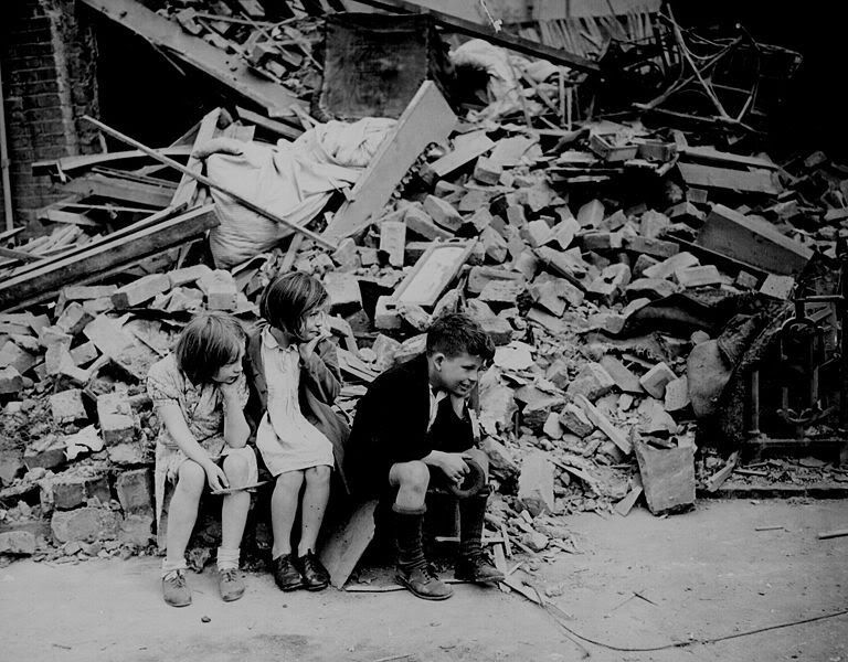 Children of an eastern suburb of London, who have been made homeless by the random bombs of the Nazi night raiders, waiting outside the wreckage of what was their home. September 1940