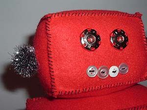Face of a robot doll made from red felt with large press studs for eyes. Image hosted by Photobucket.com