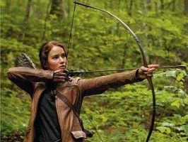Katniss pulls back the string of her bow, pointed to an object offscreen