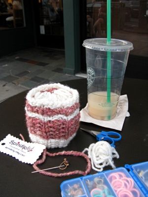 An ice cream pint cozy in pink and cream with a ball of yarn stuffed into it to hold its shape, an empty Starbucks iced drink cup, and a knitting notions box.