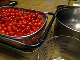 A colander full of cherries, a large steel pot, a 4 cup pyrex measuring cup, and a paper clip.