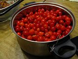 The large pot full to within an inch of the top with cherries, with a paperclip bent open into an 'S' shape hooked over the lip of the pot.