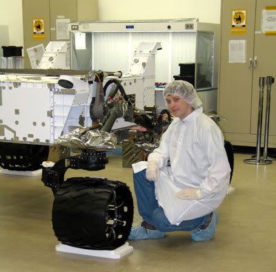 An engineer poses next to one of the wheels on the MARS SCIENCE LABORATORY.