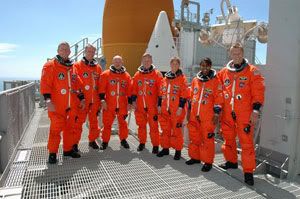 The crew of Space Shuttle Discovery poses at Launch Pad 39B with the external fuel tank and a solid rocket booster in the background.