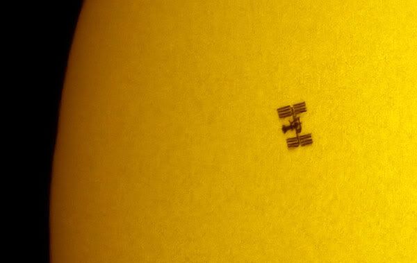 A wide shot of space shuttle Endeavour and the International Space Station in transit in front of the Sun.