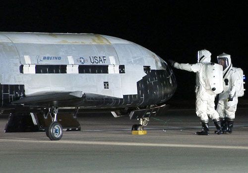 Two technicians wearing hazmat suits conduct a post-landing checkout on the OTV after its return home from space on December 3, 2010.
