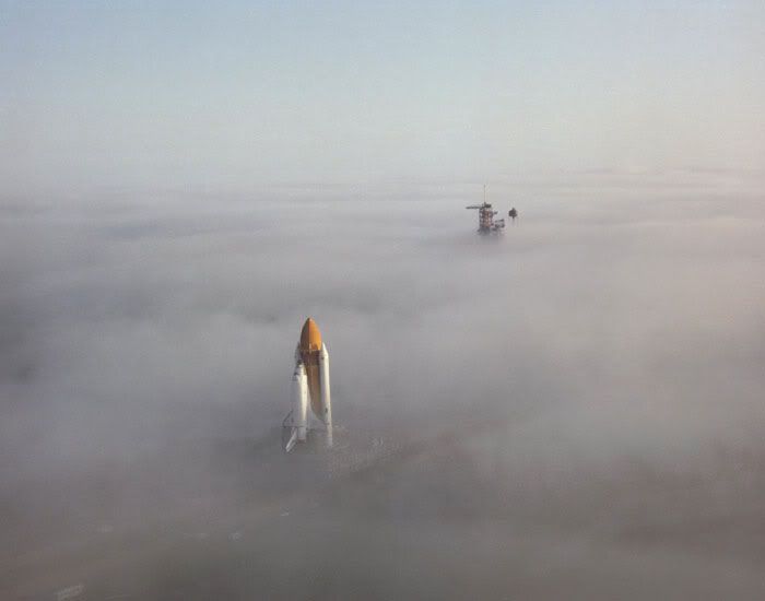 A space shuttle rolls through morning fog on its way to the launch pad.