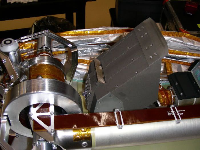 This pic shows the Robotic Arm (RA) scoop prior to launch.  To the right of the scoop (towards the upper part of the photo) is the foil-like protective barrier that shields the RA from microbial contaminants that may have hitched a ride onboard the spacecraft.
