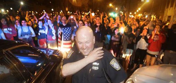 Upon hearing that the second Boston Marathon bombing suspect was taken into custody, a police officer grins while the crowd cheers behind him in a Boston suburb...on April 19, 2013.
