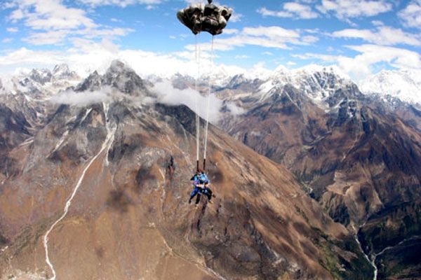 The parachute deploys as the tandem skydivers are about to land at a drop zone located in the middle of the Himalaya Mountains.