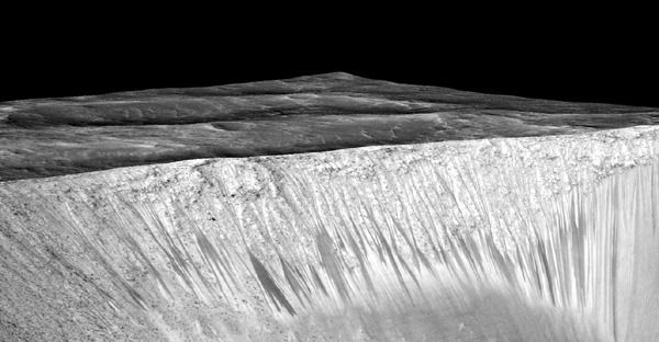 Dark narrow streaks called recurring slope lineae—thought to be formed by the flow of salty liquid water—emanate from the walls of Mars’ Garni crater in this image taken by NASA’s Mars Reconnaissance Orbiter.