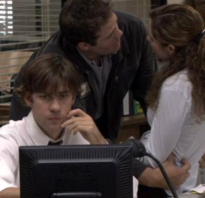 Jim Halpert pretends to be hard at work at his computer while Pam Beesly and her fiance Roy Anderson get touchy-feely behind him in THE OFFICE.