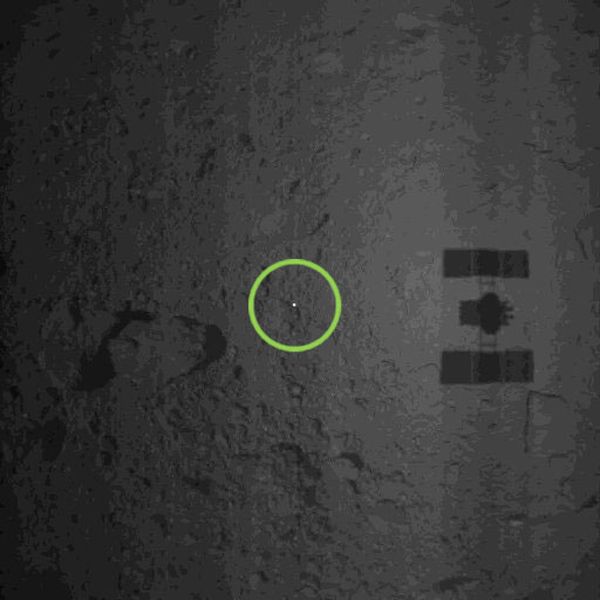 Hayabusa2's shadow is visible on the surface of Ryugu after a target marker (the white point inside the green circle) containing the names of 180,000 people successfully landed on the asteroid...on October 25, 2018 (Japan Time).