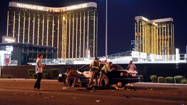 Police officers and regular citizens take cover behind a cop car after a gunman opened fire on a country music concert in Las Vegas...on October 1, 2017.
