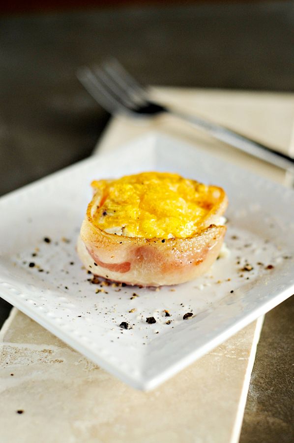 baked eggs wrapped in bacon on a white plate with a brown background