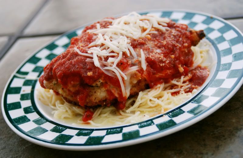 A green checkered plate with a dish of chicken parmesan over spaghetti noodles