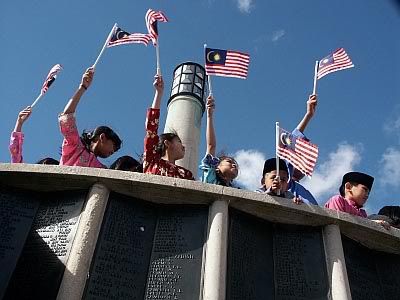 Malaysian children waving flags over the memorial plaque to those lost at sea during WWII.
