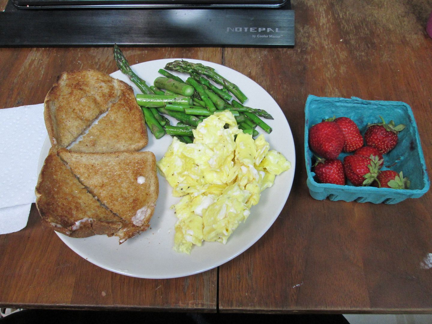 plate with toast, scrambled eggs, sauteed asparagus, next to container of strawberries