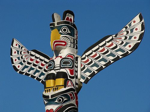 image of a carved wooden totem pole featuring a thunderbird, set against a blue sky