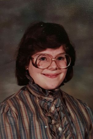 image of me at 10 years old, with a dowdy haircut, ruffled plaid blouse, and oversized glasses frames