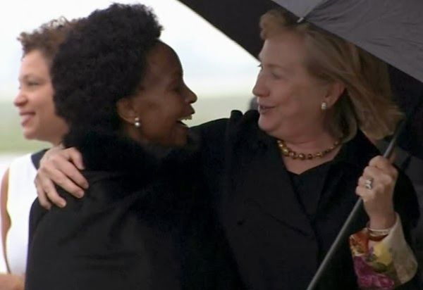 image of Hillary Clinton standing under an umbrella with her arm around Maite Emily Nkoana-Mashabane, South Africa's Minister of International Relations and Cooperation, a thin black woman