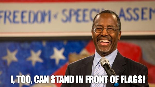 image of Ben Carson, a middle-aged black man, standing in front of a US flag