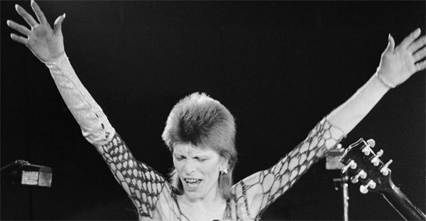 black and white image of David Bowie performing decades ago, with his arms in the air