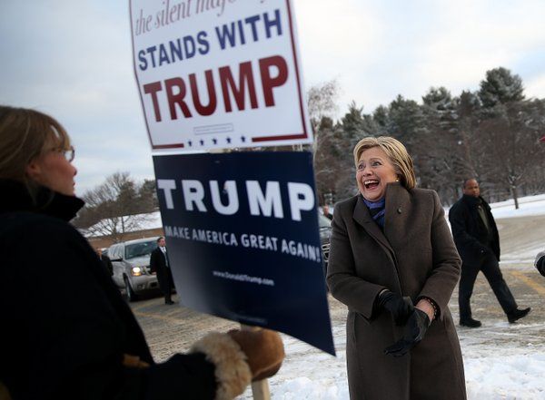 image of Hillary Clinton standing outside on a cold day, laughing at a sign being held by someone reading 'The silent majority stands with Trump'