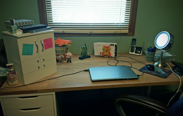 image of my desk, with a closed laptop, phone, mirror, desktop items, and toys on it