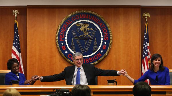 image of Tom Wheeler, an older white man, holding hands with FCC Commissioners Mignon Clyburn, a black woman, and Jessica Rosenworcel, a white woman