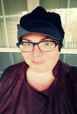 image of me sitting on the deck, wearing a grey cap, blue tortoiseshell glasses frames, and a burgundy moto jacket