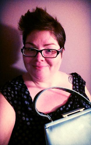 image of me in a purple room, wearing a polka dot cap-sleeved top (dark blue with light blue polka dots) and holding a light blue vintage purse