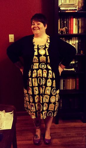 image of me in a patterned dress, featuring cats in picture frames, a black cardigan, and purple flats