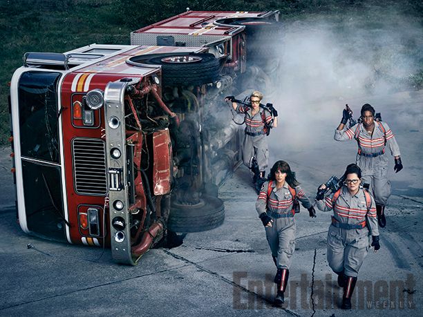 image of Kate McKinnon, Kristen Wiig, Melissa McCarthy, and Leslie Jones in costume, running past an overturned and smoking firetruck