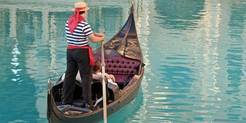 image of a man steering a gondola over crystal blue water