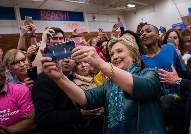 image of Hillary Clinton, standing in front of a crowd, taking a selfie