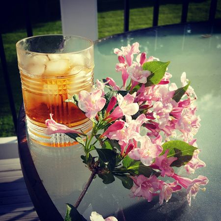 image of some flowers sitting on an outdoor table next to a glass of amber booze