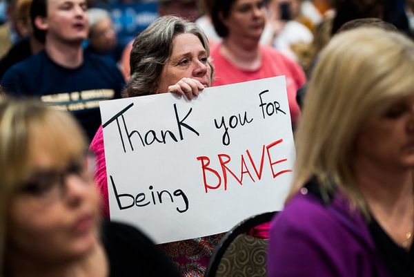 image of an older woman, who appears to be white, at a Hillary Clinton rally holding up a sign reading: 'Thank you for being BRAVE'