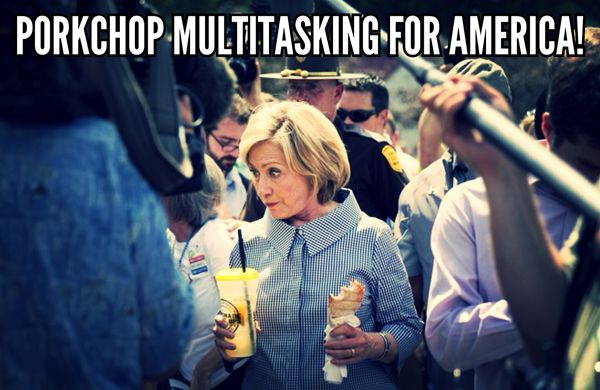 image of Hillary Clinton in a crowd at the Iowa State Fair, wide-eyed while listening to someone and holding a lemonade in one hand and a porkchop-on-a-stick in the other, to which I've added text reading: 'Porkchop multitasking for America!'
