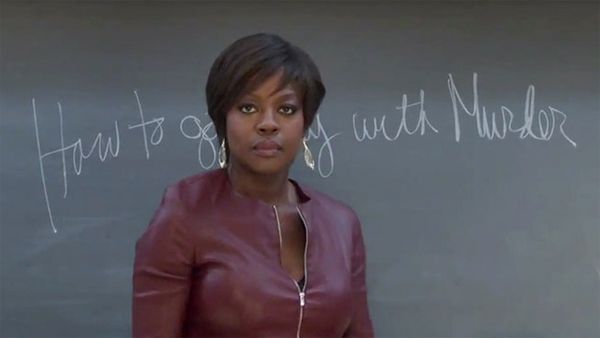 image of actress Viola Davis, a thin, black, middle-aged woman, wearing a burgundy moto jacket and standing in front of a chalkboard on which is written in chalk the name of the show