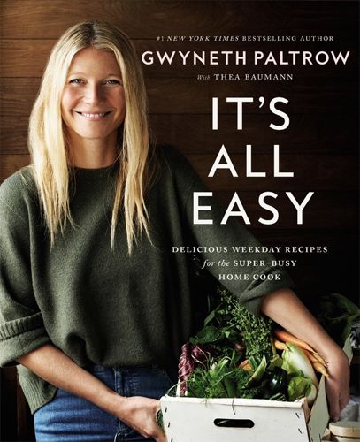 image of the cover of Gwyneth Paltrow's upcoming cookbook featuring a picture of her wearing a loose sweater and smiling while holding a basket of vegetables