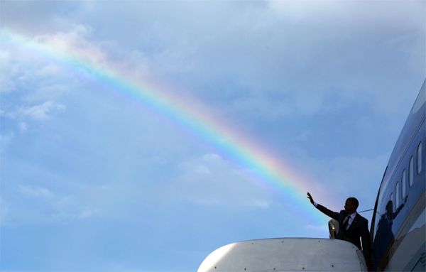 image of the President just about to board Airforce One, waving, with a rainbow behind him; the angle of the photograph makes it look as though he's casting the rainbow with his hand