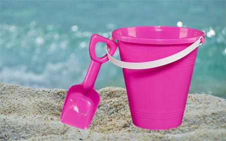image of a pink sand pail and shovel sitting in the sand on a beach