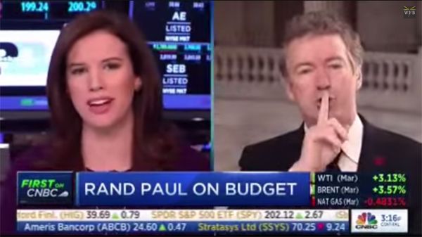 screen cap of a split-screen interview between CNBC Anchor Kelly Evans and Senator Rand Paul; Evans has an incredulous look on her face as Paul has his fingers to her lips, shushing her