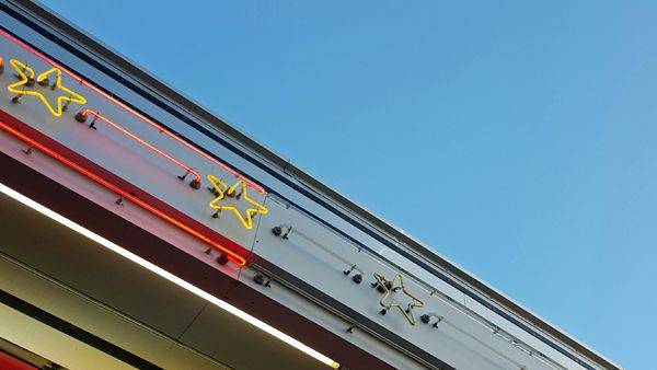 image of the eaves of a restaurant's roof, with yellow and red neon light designs, against a bright blue sky