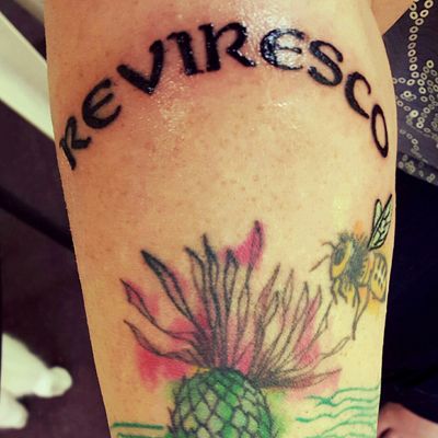 image of my forearm on which is viewable just the top part of my tattoo of a thistle and a bee, with the newly added bee wing and text reading REVIRESCO