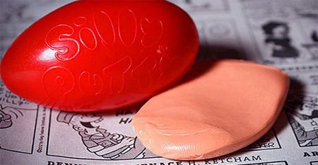 image of the classic red egg-shaped Silly Putty container, with a glob of Silly Putty sitting beside it on the comics section of a newspaper
