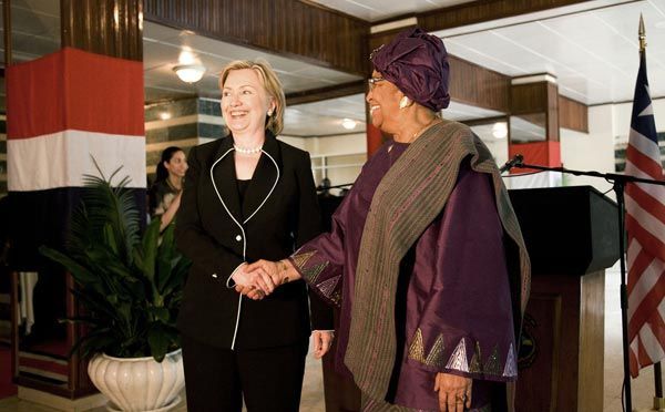 image of Hillary Clinton with Ellen Johnson Sirleaf, President of Liberia, an in-betweenie black woman; they are standing beside each other smiling and shaking hands